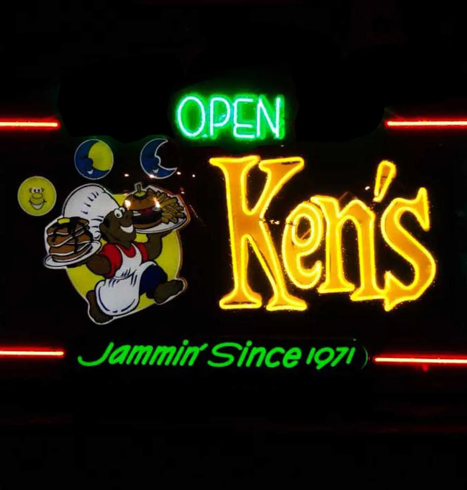 Ken's House of Pancakes neon roadside sign glowing at night, reading OPEN, Ken's, and Jammin' Since 1971, with a cartoon chef mascot balancing plates of pancakes and a burger with fries
